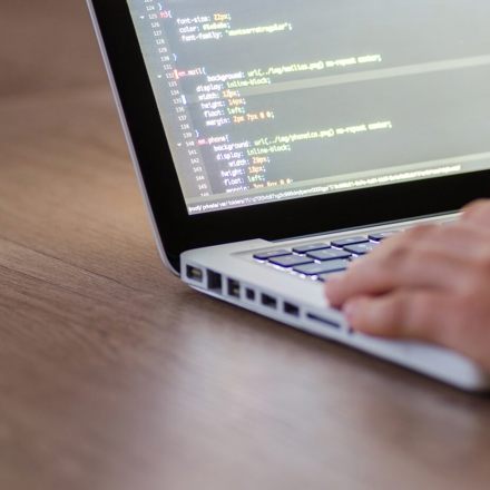 Hand resting on a laptop. Screen showing code. 