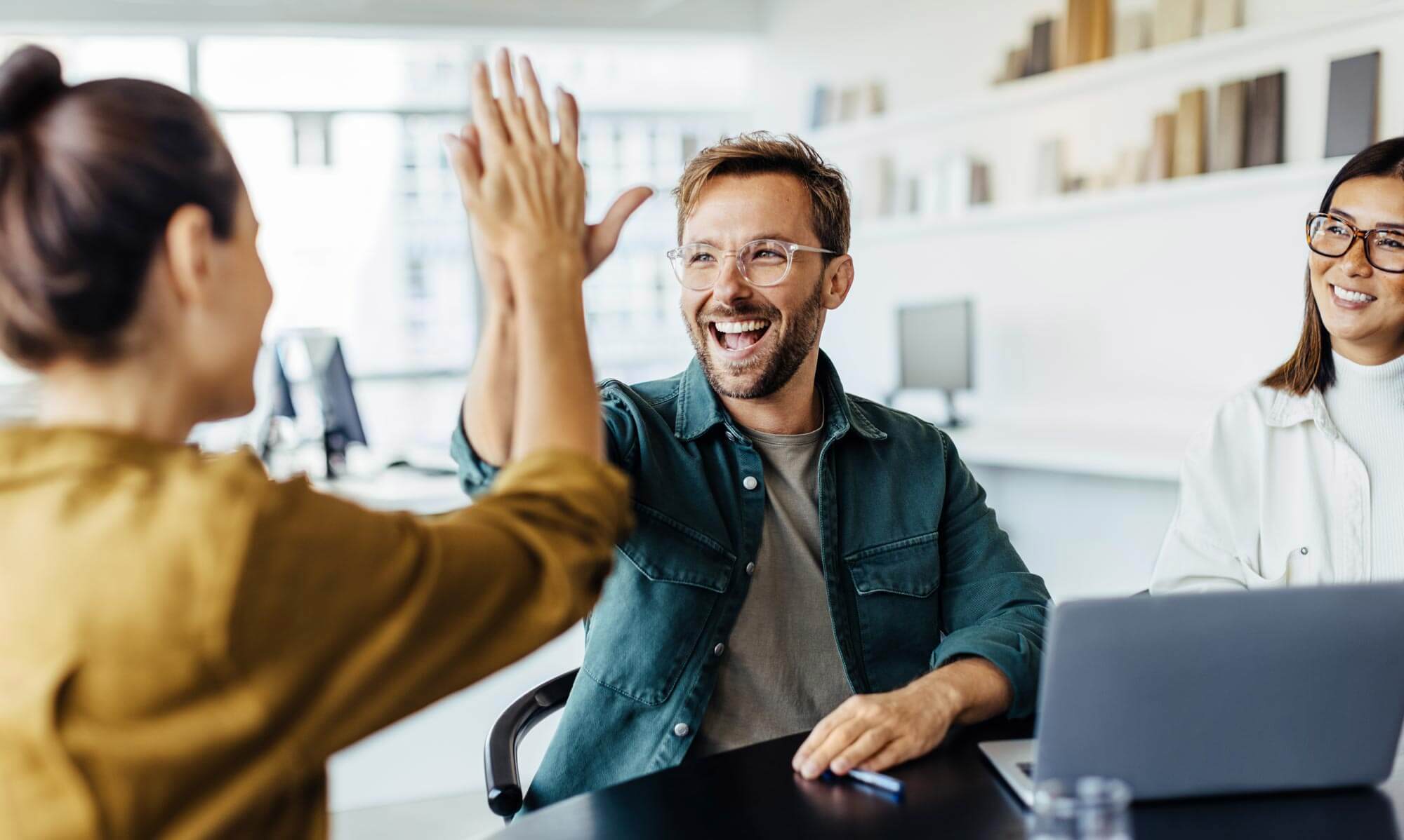 Successful business people giving each other a high five in a meeting. Two young business professionals celebrating teamwork in an office.