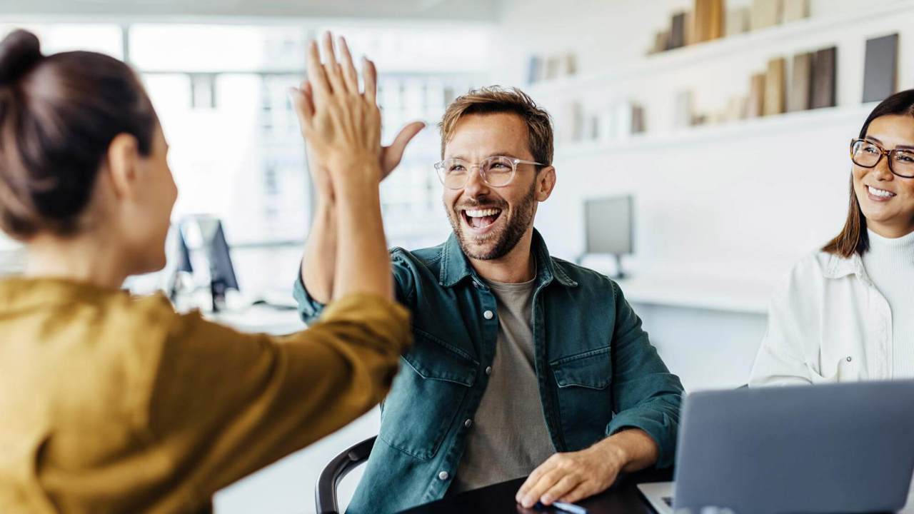 Successful business people giving each other a high five in a meeting. Two young business professionals celebrating teamwork in an office.