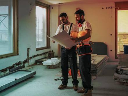 Full length of construction workers analysing blueprints in the apartment.